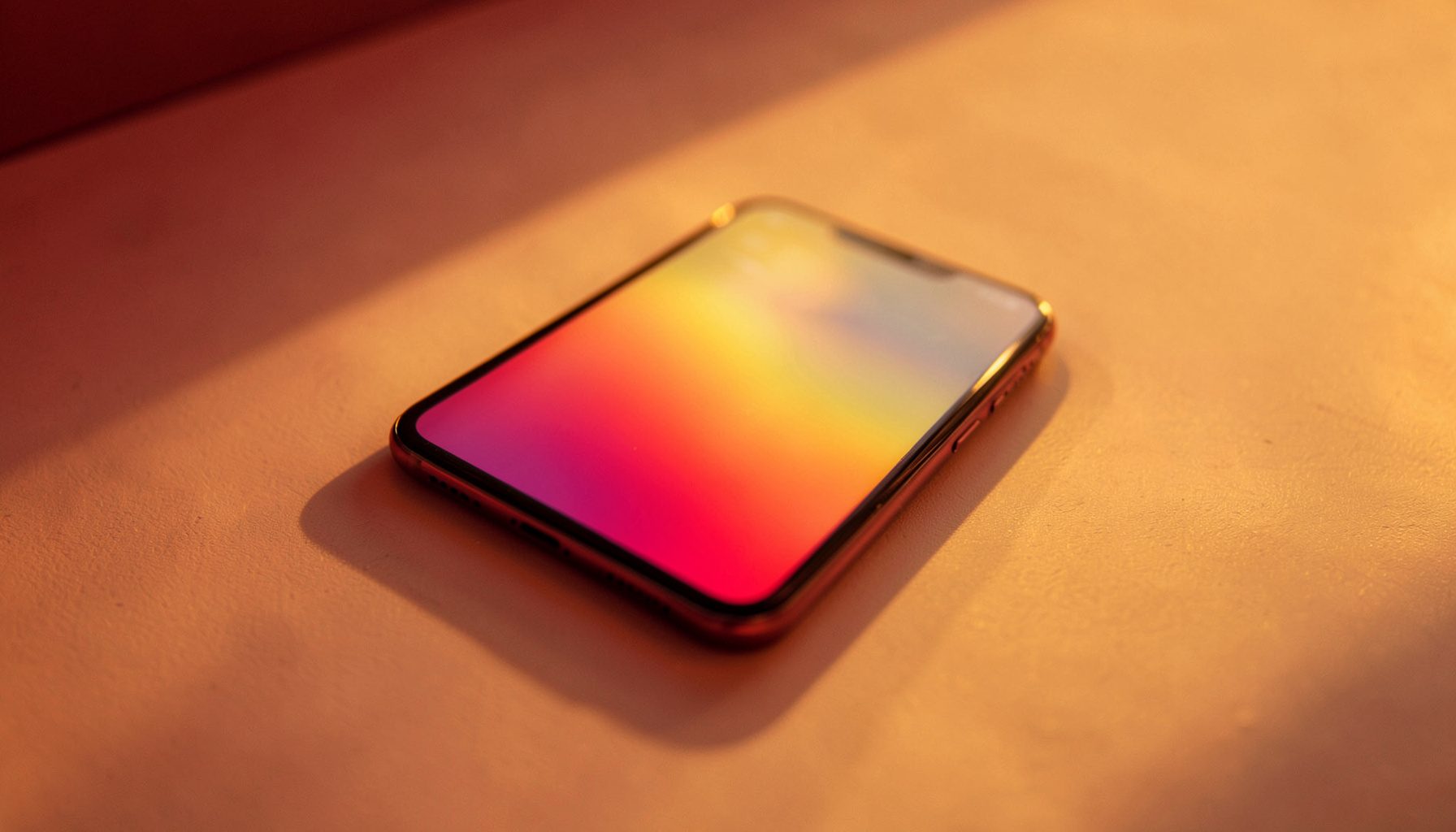 Smartphone with a vibrant gradient display in warm golden-hour light on a minimalist surface