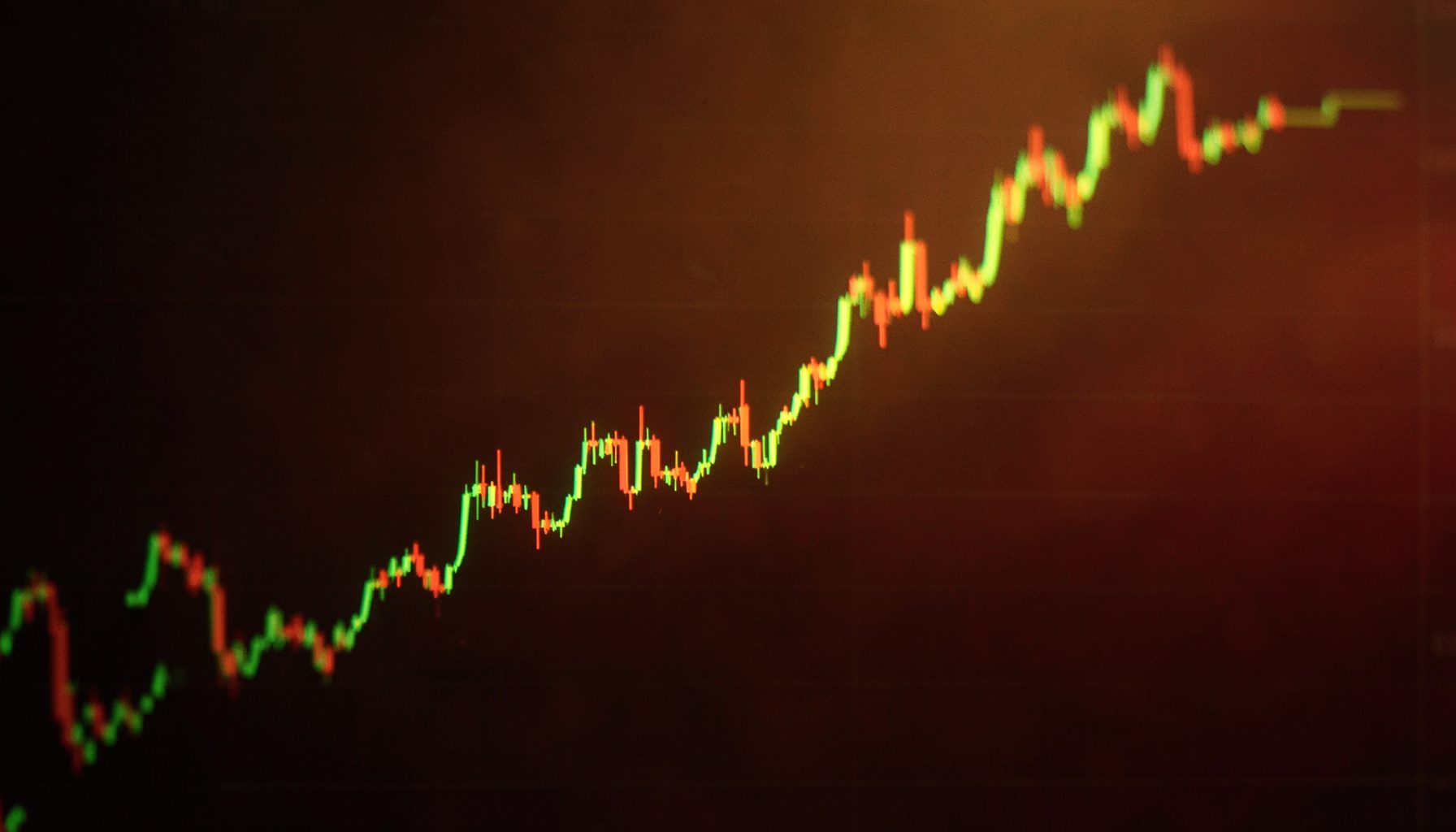 A stock chart line trending upward on a dark screen, warm amber and green highlights.